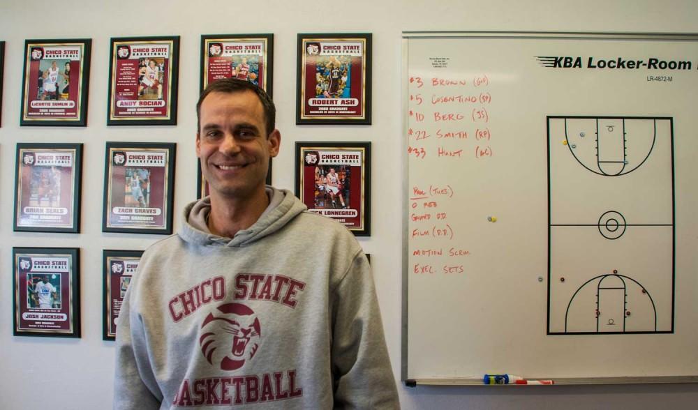 Chico State mens basketball coach Greg Clink poses in front of his former players plaques. Photo credit: Alex Boesch