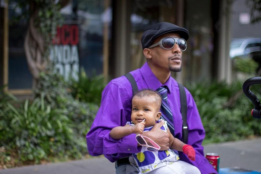 Jamari Caldwell sits with his daughter at the Thursday Night Market during the spread of Paint the Town Purple. He is supporting Relay for Life by wearing purple to raise awareness for the fight against cancer. Photo credit: Maisee Lee