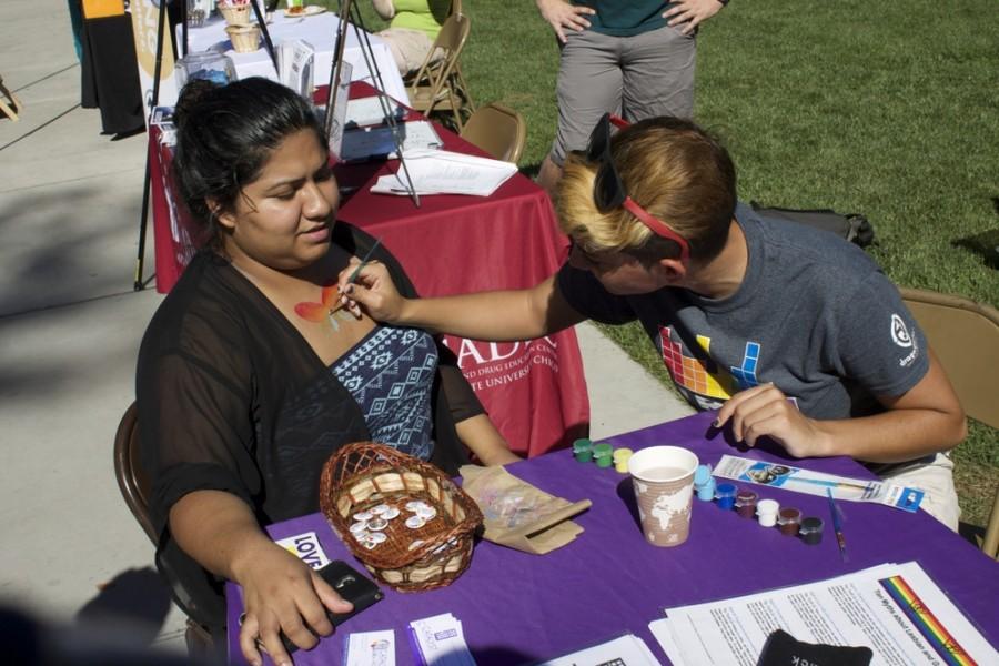 Catalyst intern, Sarena Kirk, paints Griselda Avila's chest in support of Queer Week 2014.