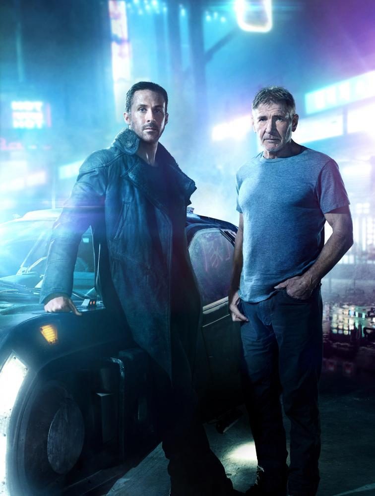K and Deckard side by side. The neon lights and futuristic-looking car compliment the setting. Image from bladerunnermovie.com