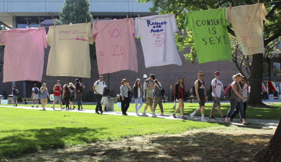 Students stop to read colorful shirts strung up throughout the trees outside the Meriam Library. The shirts are the work of students who participated in the Chico State Clothesline Project last week by making shirts at the BMU. The shirts are hung across campus as a visual reminder of sexual assault and domestic violence statistics that we often ignore. Photo credit: Anne Chamberlain