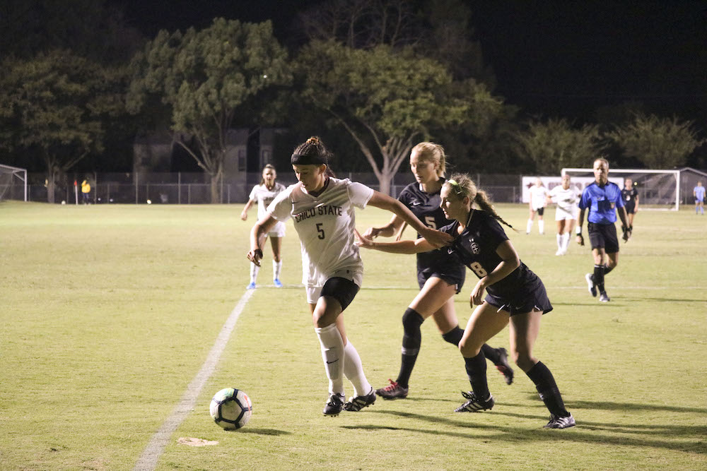 Kyra Greenwood kicks the ball as two Azusa players run after her. Photo credit: Melissa Herrera