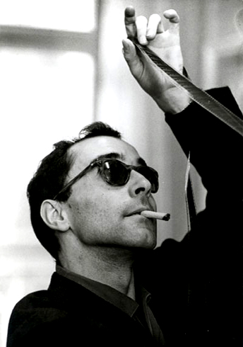 Jean-Luc Godard examining a reel of film while smoking.