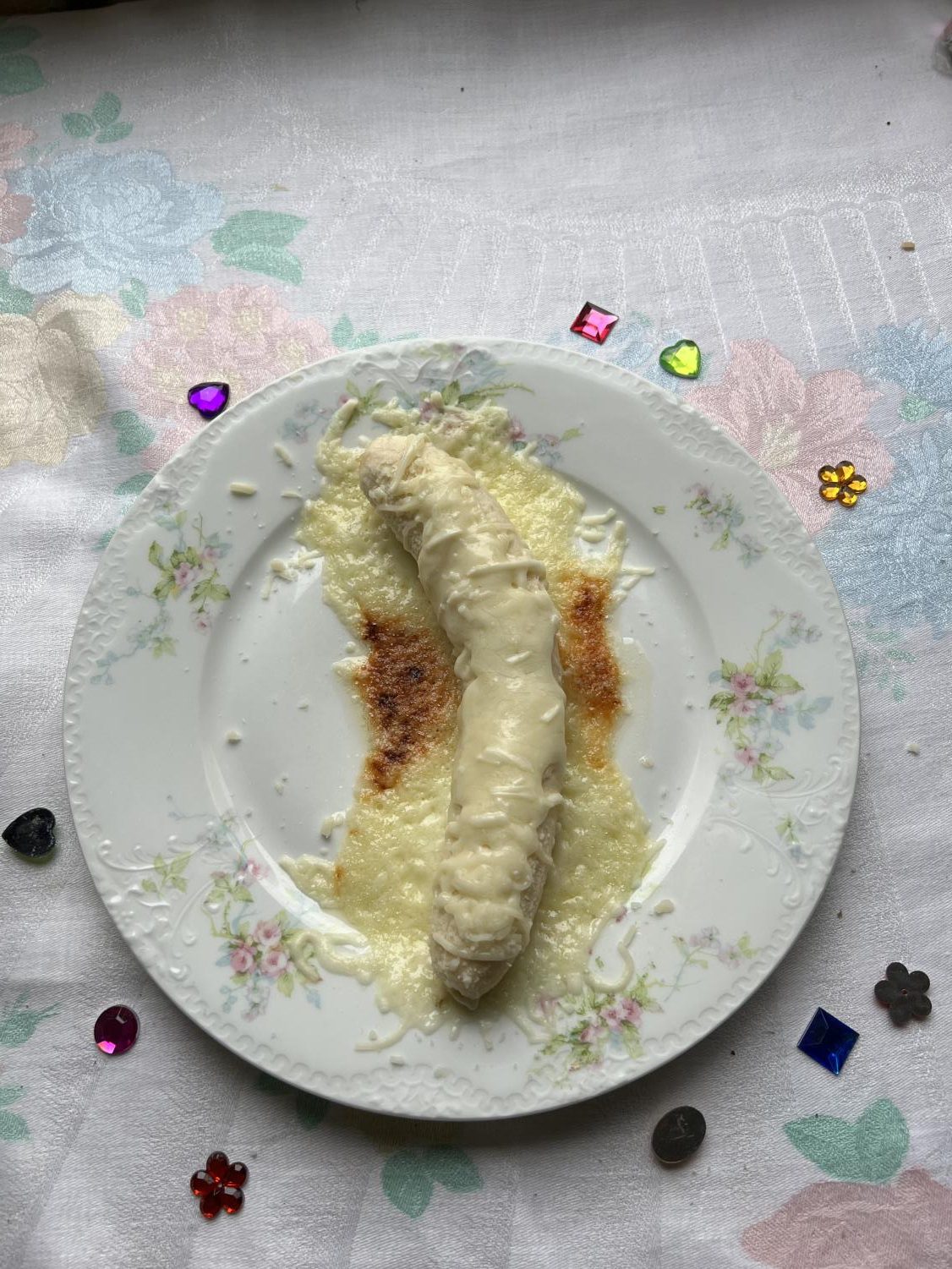 banana with melted cheese on top. white plate and white flowery table cloth