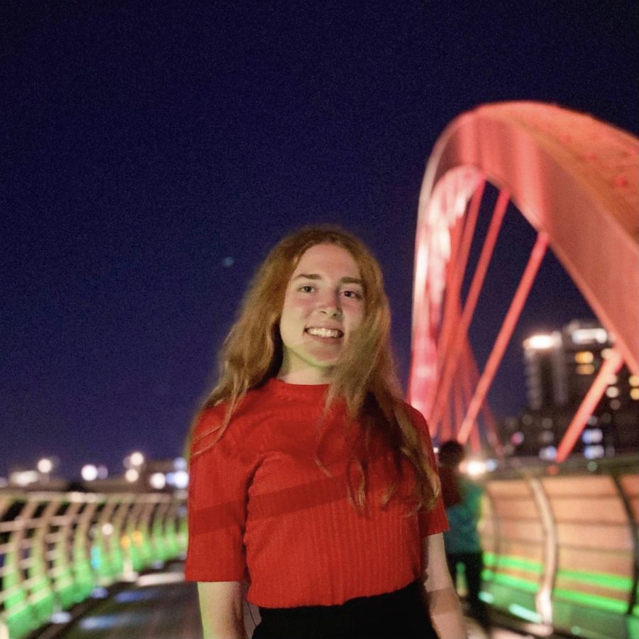 Girl in red shirt stands in front of a city at night