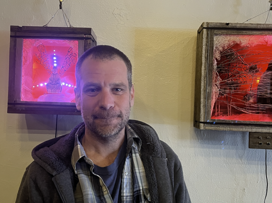 Zak Elstein stands near two of his shadow boxes hanging in The Naked Lounge.