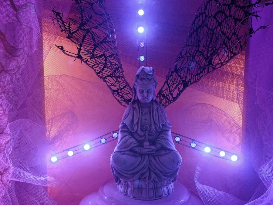 An idol rests in the middle as the centerpiece, two makeshift wings stretch our from its back. Three LED arms with five lights each act as a backdrop casing soft pink and purple hues. White lace and sheers surround the centerpiece.