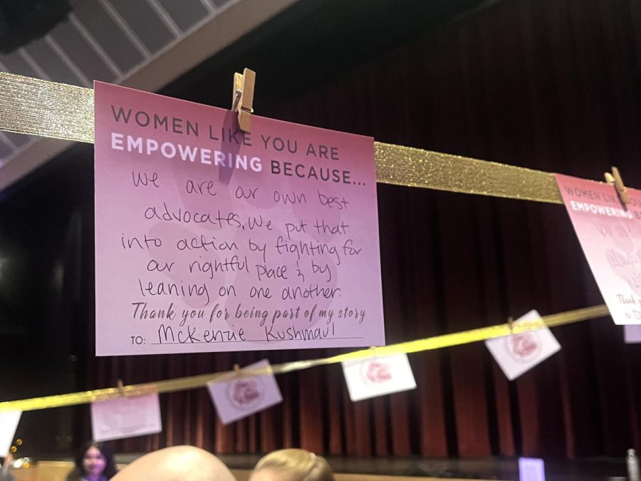 A purple card addressed to McKenzie Kushmaul and says "We are our own best advocates, we put that into action by fighting for our rightful place and by leaning on one another" hangs on a golden ribbon.