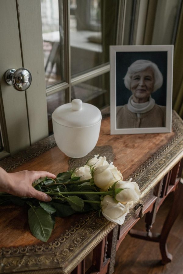 Table with a photo of an elderly woman, a cremation urn, and a hand placing flowers.