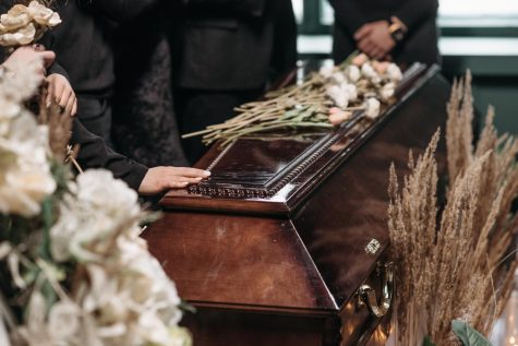 Hands placed on a wooden casket with flowers