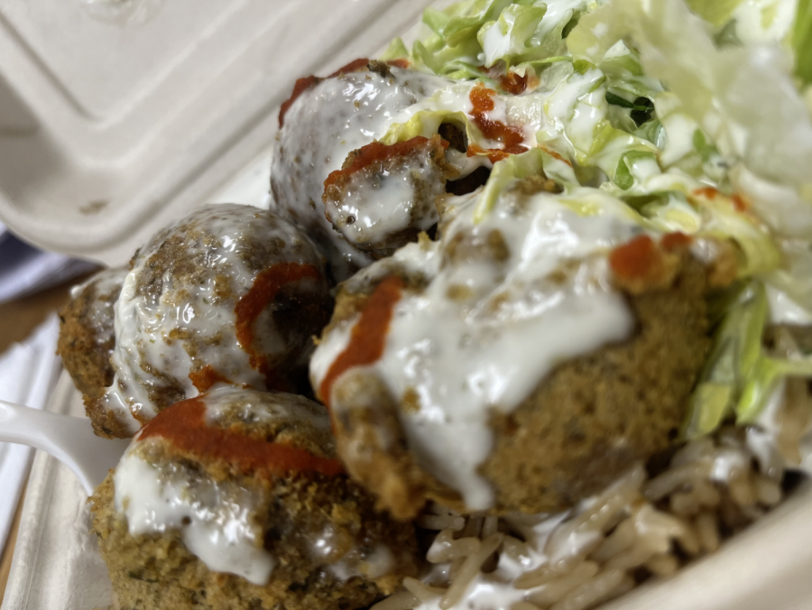 Four falafel balls covered in white and red sauces sit on-top of rice and next to lettuce.