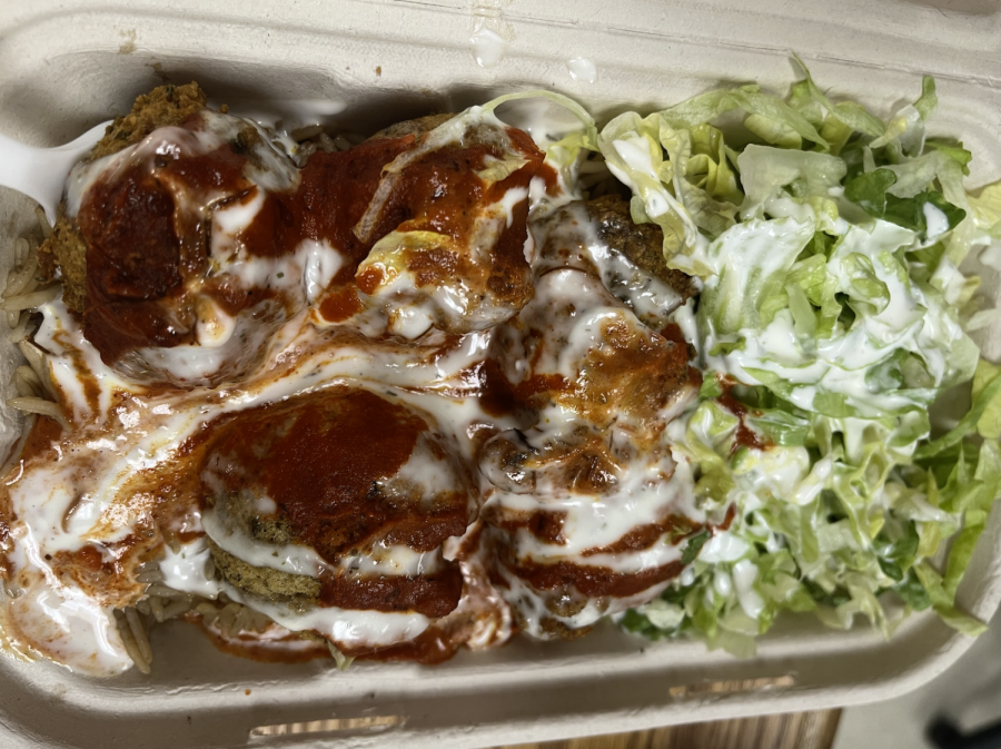 Four falafel balls sit on-top of rice and lettuce, covered in white and red sauces.