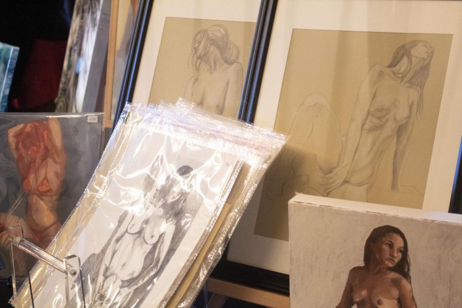 Two framed prints depicting posed nude women it behind plastic surrounded prints available for buyers to leaf through.
