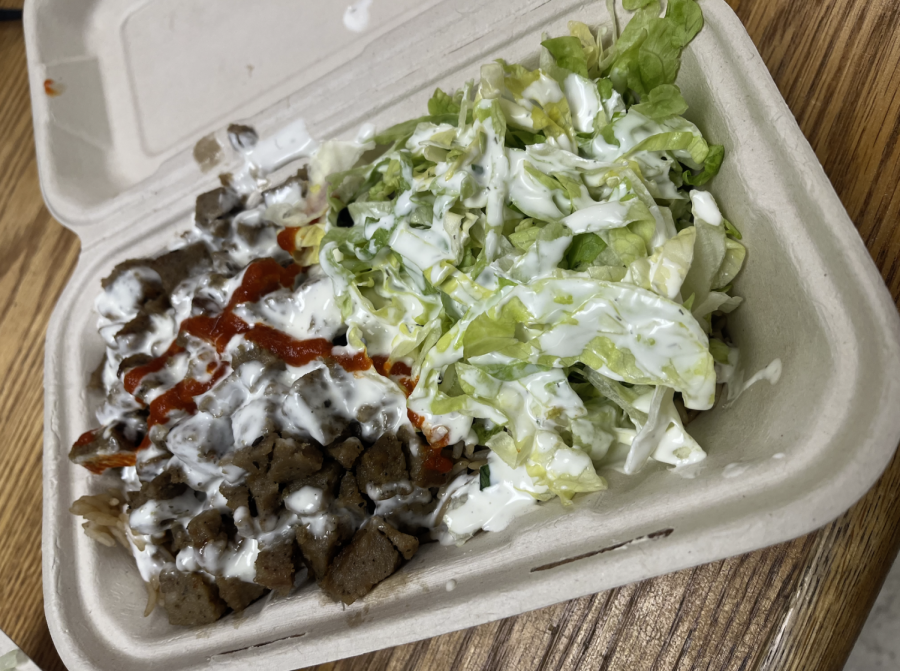 Lamb sits in one half of the paper container, lettuce in the other, all on-top of a bed of rice.