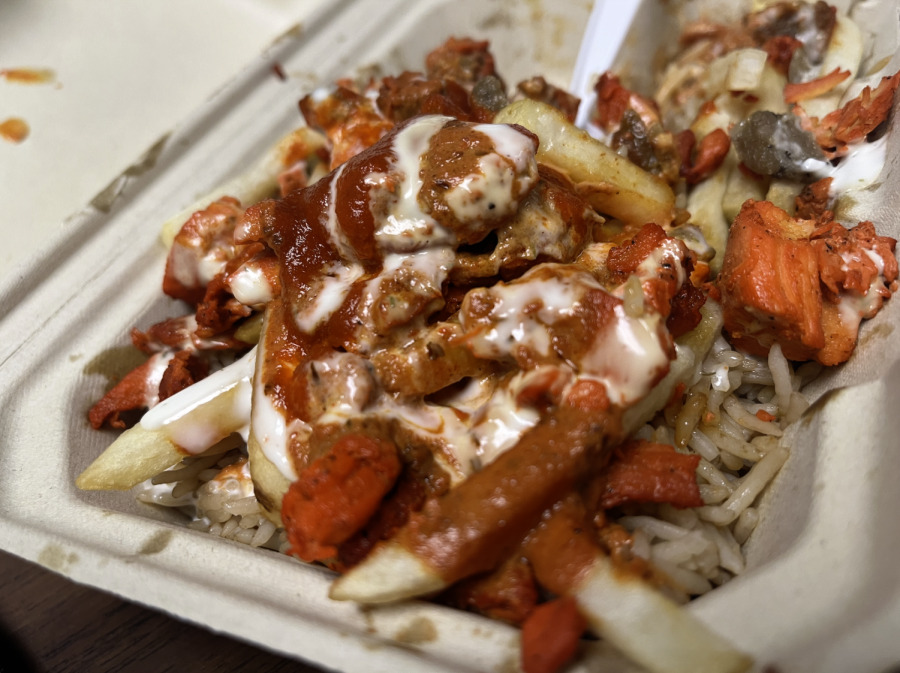 Fries sit on-top of a bed of rice covered in white and red sauces.