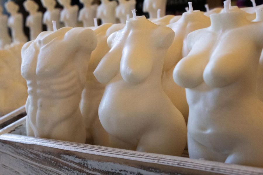 Three types of white candle sit in rows on a wooden tray. On the far left is an abed nude bust, in the middle is a pregnant nude bust and on the far right is a breasted nude bust.