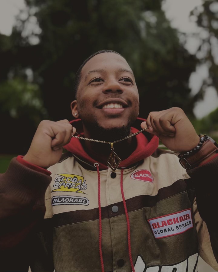 Male seemingly smiling while holding his chain and also wearing NASCAR jacket