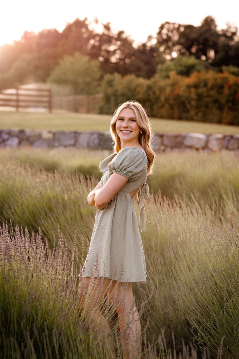 Juliet smiling and standing in a lavender field, wearing a green dress.