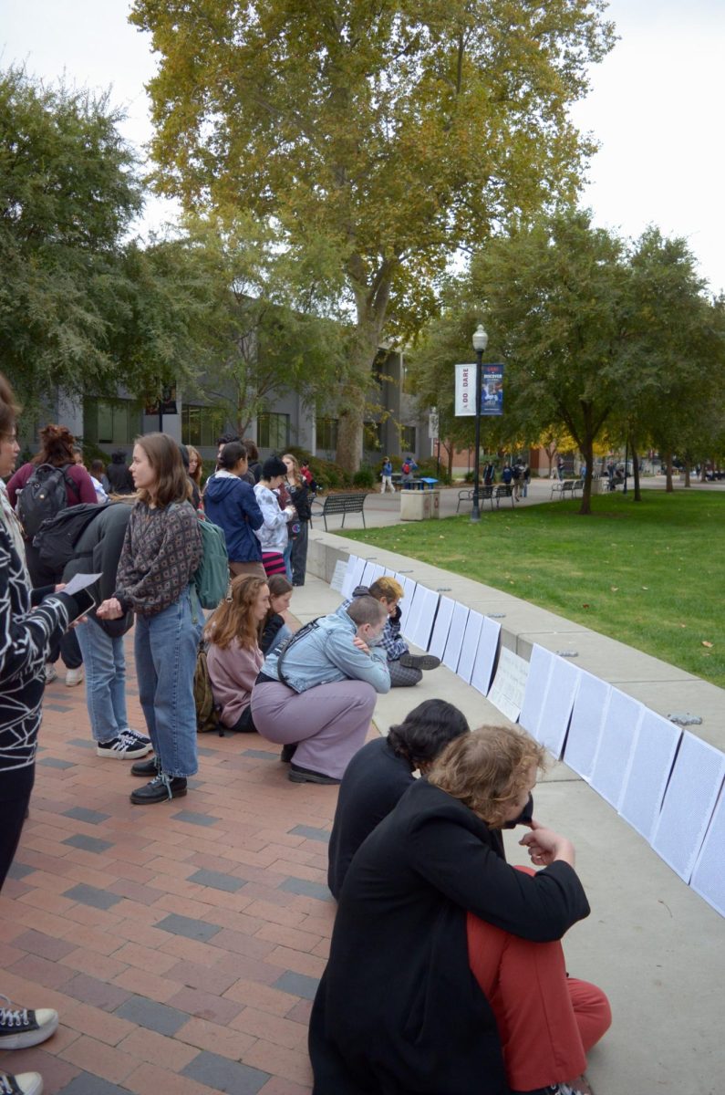 Students kneel on the sidewalk to read the names of Palestinian victims.