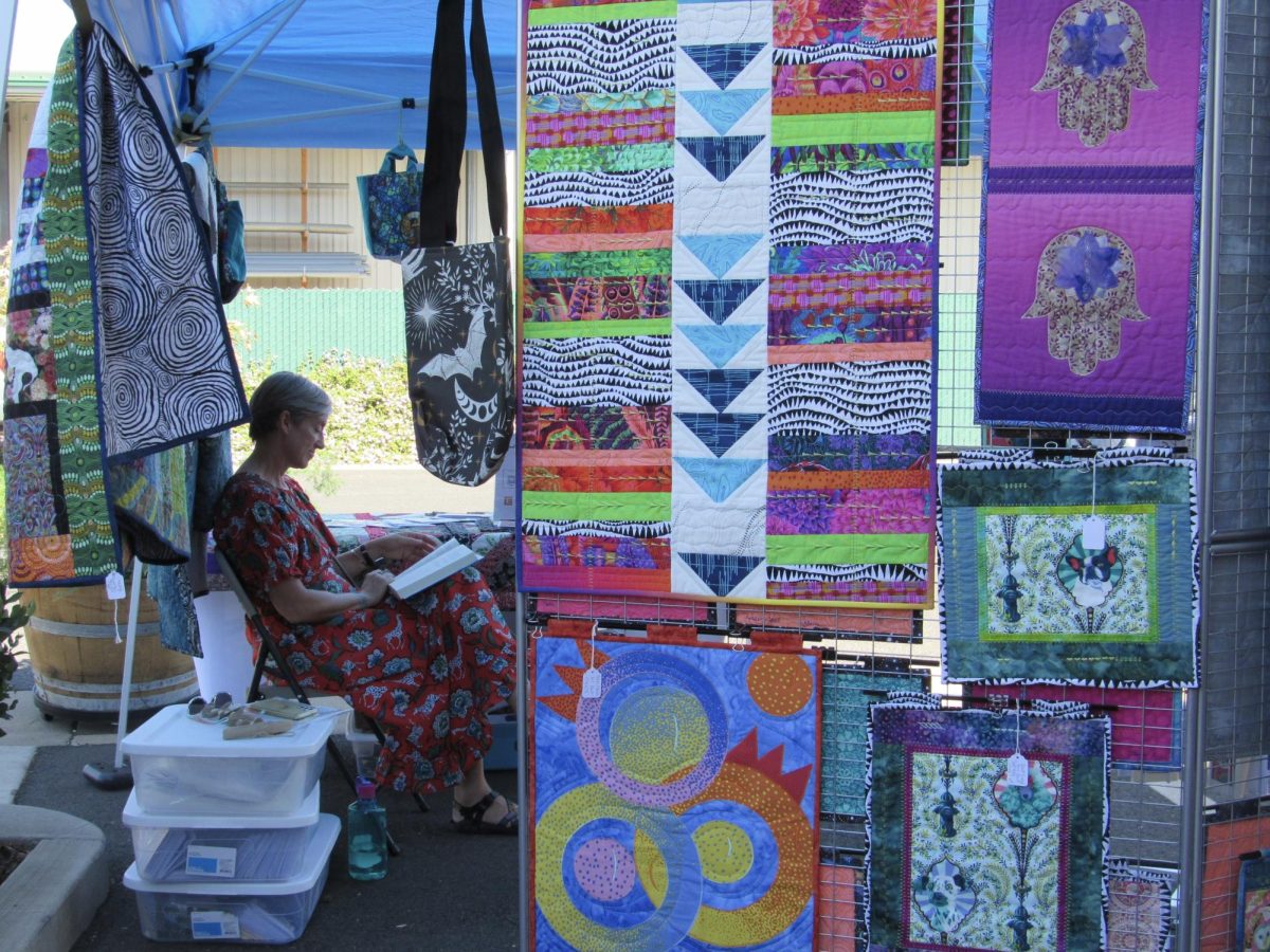 Elaine Ellismore, a teacher in Chico who does quilting and fabric art, reads a book while waiting for customers at Blossom Pop-Up market on Sunday. Her business, Sewed Up by Elaine, focuses on creating quilts that "tell a story". Photo by Megan Gauer on Sept 29. 